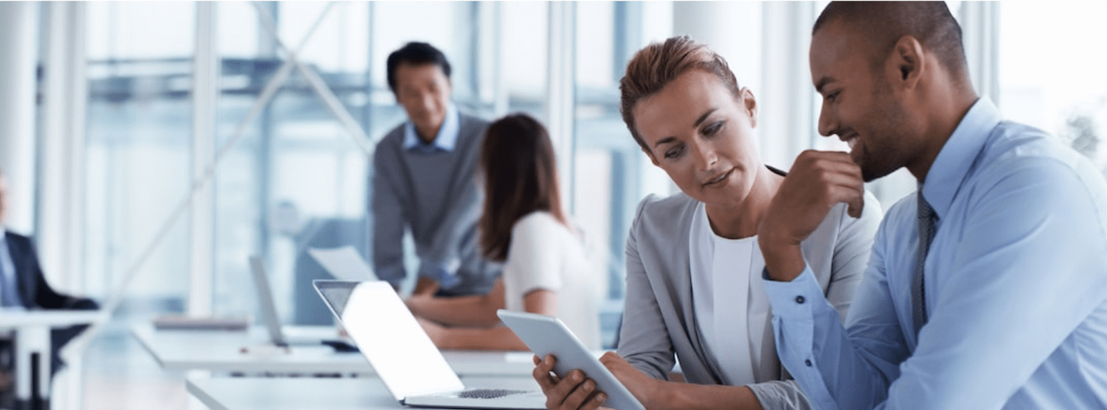 Two businesspeople discuss something while one person navigates on their mobile phone. Two other business people in the background also discuss something.