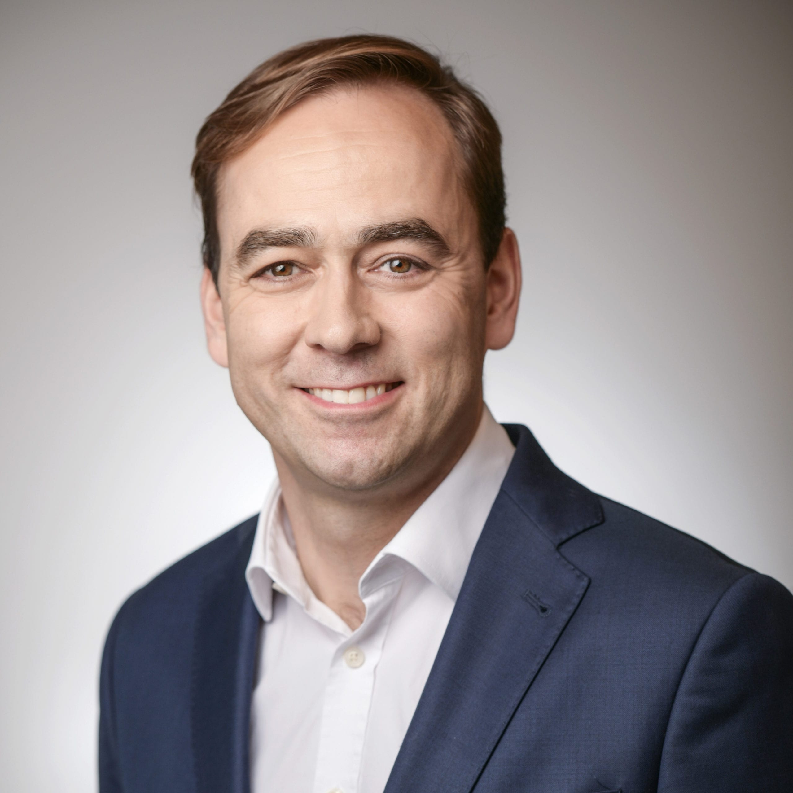 Headshot of a man smiling and wearing a navy suit with a white shirt.