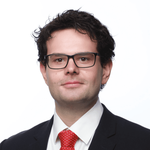 Headshot of Alex Eade wearing glasses and a suit