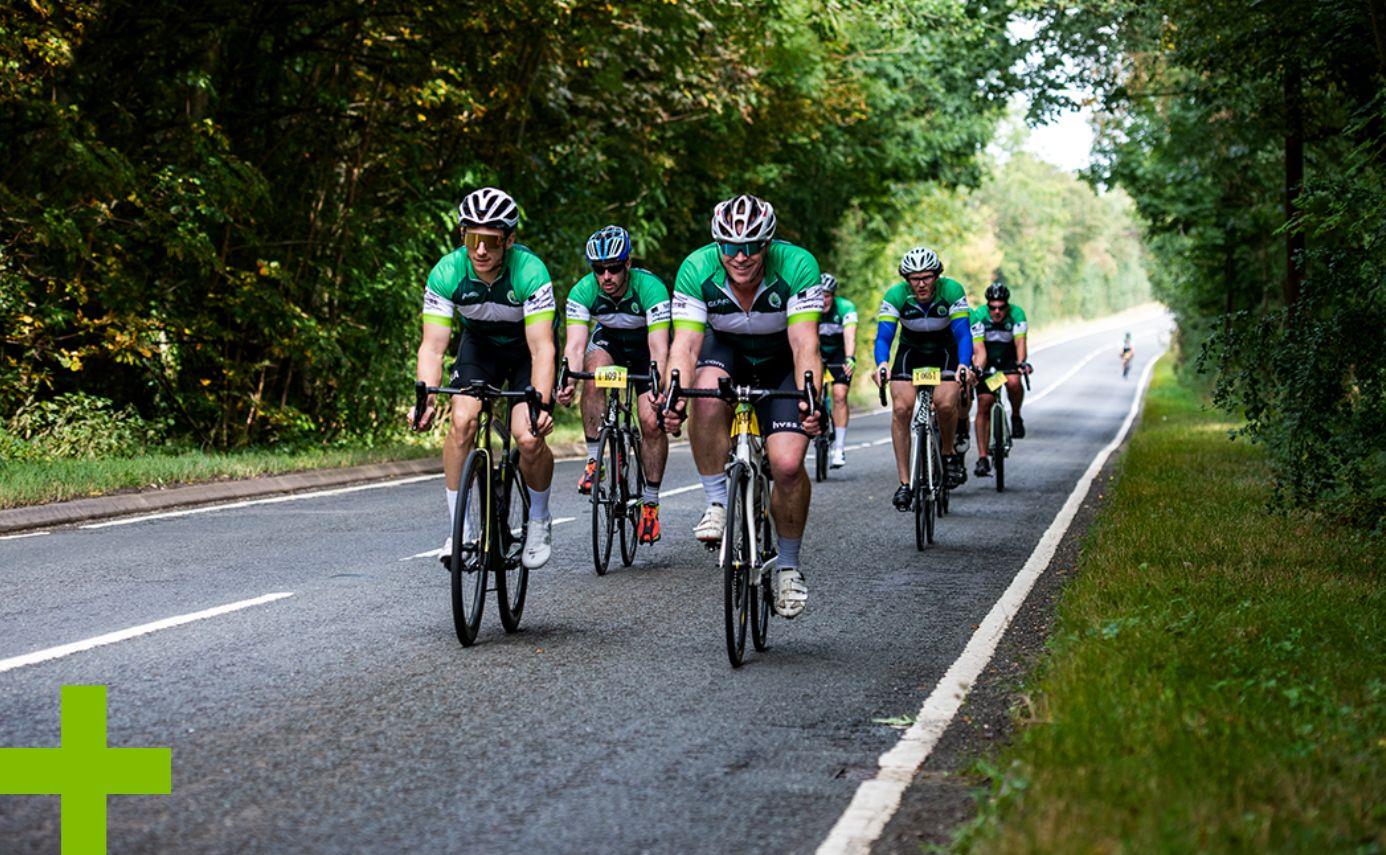 Peleton of GLP employees on bicycles riding down a road together.